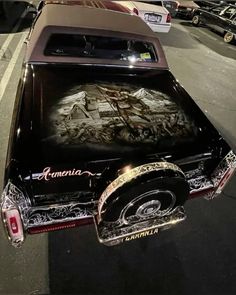 an old car parked on the side of the road with its hood covered in graffiti