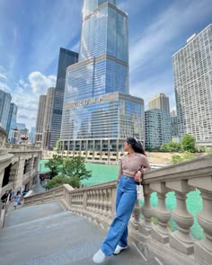 a woman standing on the side of a bridge next to tall buildings in a city