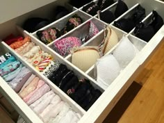 an organized drawer with clothes and bras in the bottom section, on top of a wooden floor