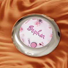 a compact mirror with the word sophka on it sitting on a satin surface