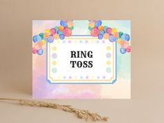 a card with the word ring toss on it and balloons around it, sitting next to a dried plant