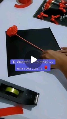 a person is cutting out red ribbon on a black piece of paper with a pair of scissors