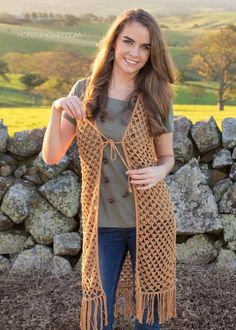 a woman standing in front of a stone wall wearing a brown knitted shawl