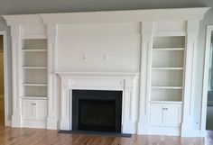 an empty living room with white bookcases and fireplace