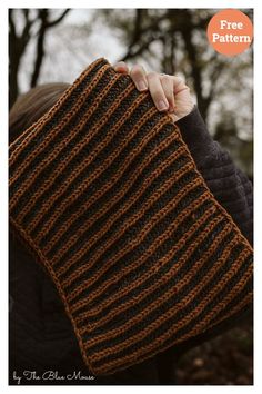 a woman holding up a brown and black knitted scarf