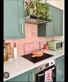 a kitchen with green cabinets and pink tile backsplashing, potted plants on the stove