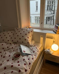 a laptop computer sitting on top of a bed next to a window with hearts on it