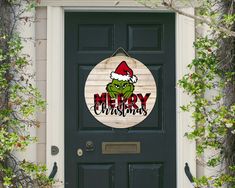 a door with a merry christmas sign hanging on it's side and green plants growing around