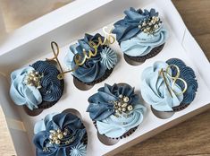 six cupcakes in a box with blue frosting and gold decorations on top