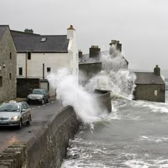 waves crashing into the sea next to some houses and cars in front of water splashing on the street