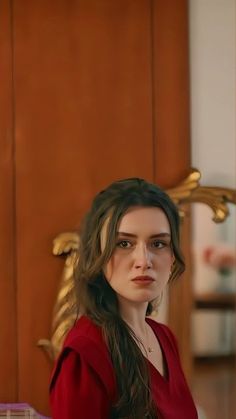 a woman in a red dress sitting on a chair looking at the camera with her eyes closed