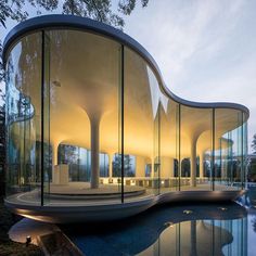 a curved building with glass walls next to a body of water