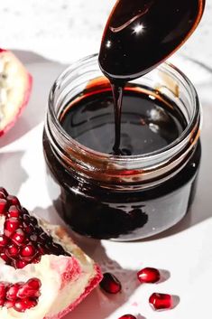 pomegranate being drizzled onto a piece of cake next to a jar of jam