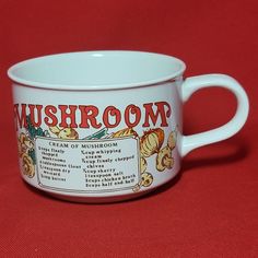 a white mug with the words mushroom on it sitting on a red tableclothed surface