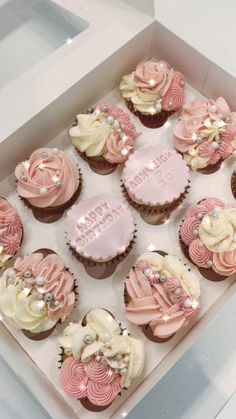 a box filled with lots of cupcakes covered in frosted pink and white icing