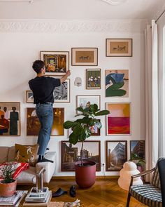 a man standing on top of a white couch in front of a wall filled with pictures