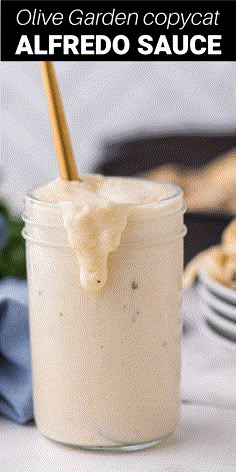 a glass jar filled with sauce sitting on top of a white table next to cookies