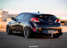 the rear end of a black sports car parked in a parking lot next to a building