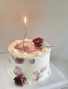 a birthday cake with a single lit candle on it and flowers around the edges, sitting on a white box