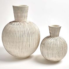 two white vases sitting next to each other on a white surface with no one around them