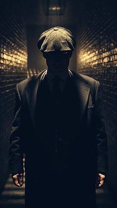 a man in a suit and hat walking down a dark hallway with his hands on his hips