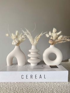 three white vases sitting on top of a book