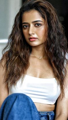 an image of a woman with long hair wearing jeans and a white tank top sitting down