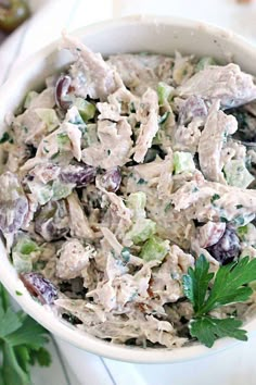 a white bowl filled with chicken salad and garnished with parsley on the side