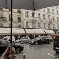 a person holding an umbrella in front of some parked cars on a city street with tall buildings