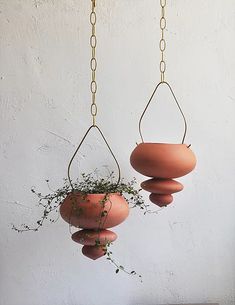 two hanging planters with plants in them on a table next to a white wall