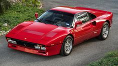 a red sports car parked on the side of a road next to grass and bushes