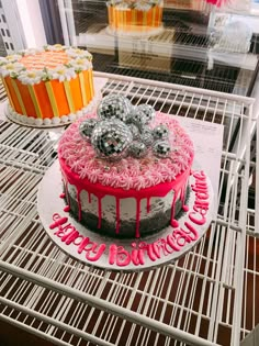 two cakes with pink icing and decorations on them sitting on a rack in a bakery