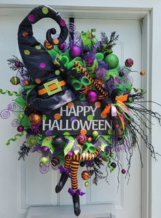 a wreath decorated with halloween decorations and witch hats is hanging on the front door to say happy halloween