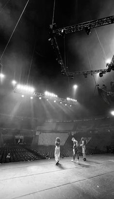 three young men playing basketball in an empty arena with lights shining on the bleachers