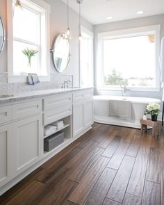 a white bathroom with wood flooring and two round mirrors on the wall above the bathtub