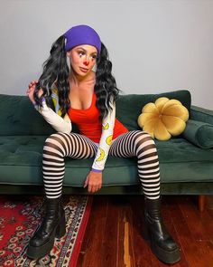 a woman sitting on top of a green couch wearing tights and stockings with clown makeup