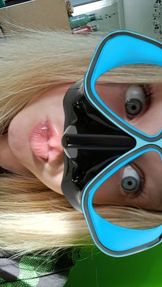 a woman with long blonde hair wearing a black and blue mask on her face, looking at the camera