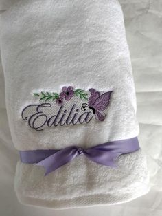 a personalized white towel with purple ribbon and butterfly on it, sitting on a bed