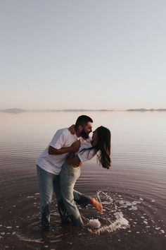 a man and woman standing in the middle of water with their arms around each other