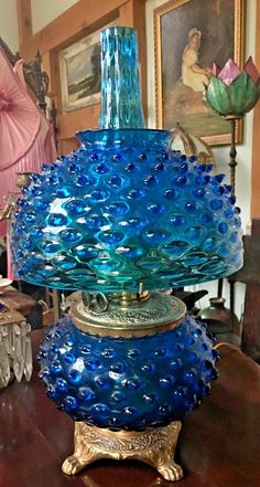 a blue glass vase sitting on top of a wooden table next to a pink lamp