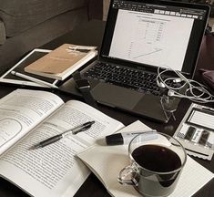 a laptop computer sitting on top of a table next to an open book and cup of coffee