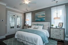 a bedroom with gray walls and white bedding, two windows, blue rugs and a painting on the wall