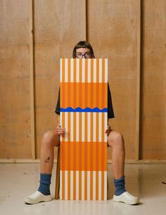 a man sitting on top of an orange and white striped chair with his legs crossed