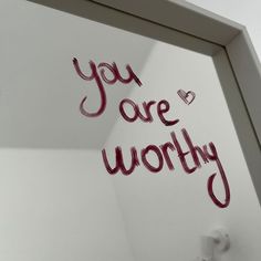 the words you are worthy written in red ink on a white wall behind a mirror