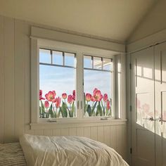 a bed sitting next to two windows in a room with white walls and wooden floors