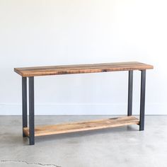 a wooden table sitting on top of a cement floor next to a white wall with black metal legs