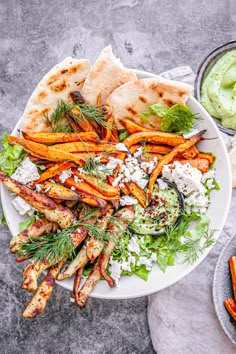 a white plate topped with carrots and pita bread next to a bowl of guacamole