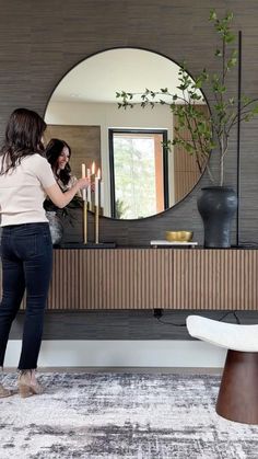 a woman is standing in front of a mirror with candles on the table next to her