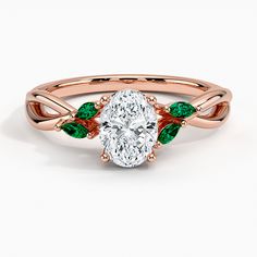 a rose gold ring with an oval cut diamond and green leaves on the band, set against a white background