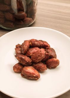 a white plate topped with almonds on top of a wooden table next to a glass jar